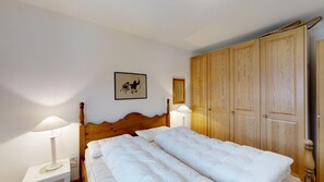 A bedroom with a wooden bed, two bedside lamps, a wooden wardrobe, and a framed picture on the wall.