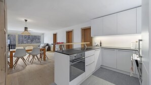 A modern kitchen with white cabinetry, a central island with a stove, and a dining area with a table and chairs.