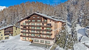A multi-story hotel with balconies, surrounded by snow-covered trees and a clear sky.