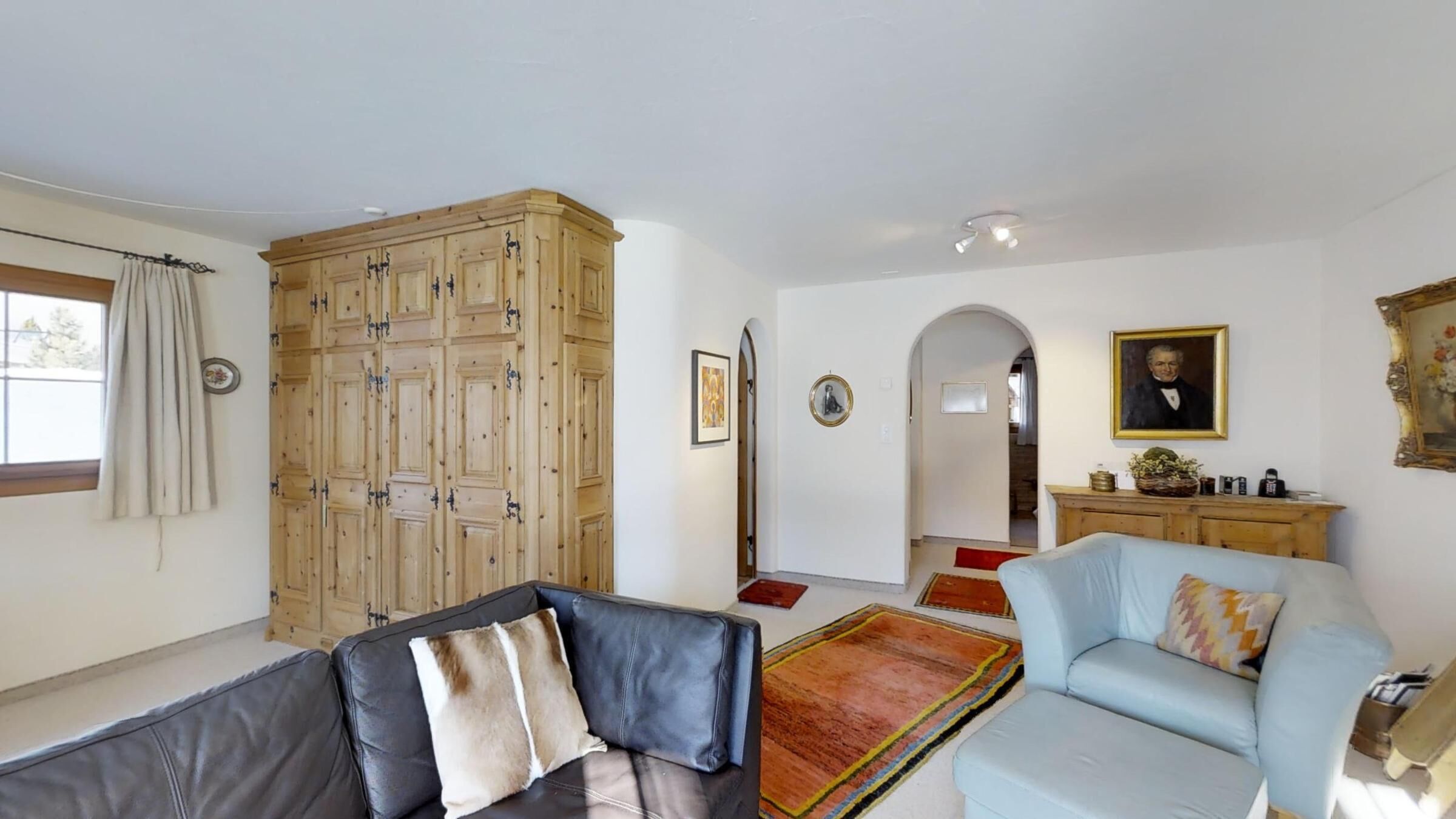 Een woonkamer met een bank, een lichtblauwe fauteuil, een houten kast en een schilderij aan de muur.