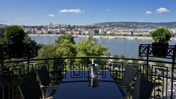 Eine Terrasse mit Tisch und Stühlen mit Blick auf einen Fluss und die Stadtlandschaft.