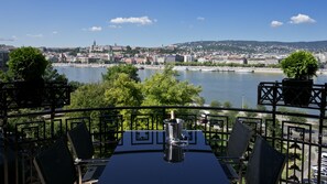 Une terrasse avec une table et des chaises donnant sur une rivière et sur le paysage urbain.