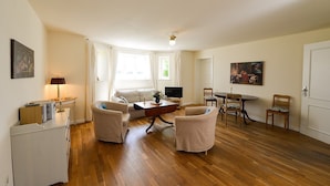 Una sala de estar con un sofá, dos sillones, una mesa de centro, un televisor y una mesa de comedor con sillas.