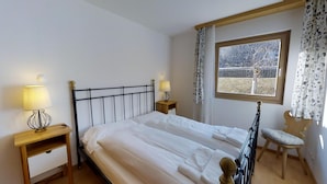 Un dormitorio con una cama, dos mesitas de noche, una ventana con cortinas y una silla.