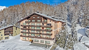 Un hotel de varios pisos con balcones, rodeado de árboles cubiertos de nieve y un cielo despejado.