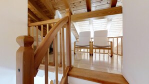 Un escalier en bois mène à une pièce où se trouvent deux chaises blanches et un plafond en pente.