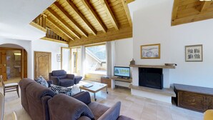 Un salon spacieux avec un haut plafond en bois, une cheminée, un téléviseur et un canapé.