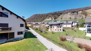 A residential area with modern houses, a paved road, and a hillside in the background. - 2-room apartment ca. (Celerina/Schlarigna)