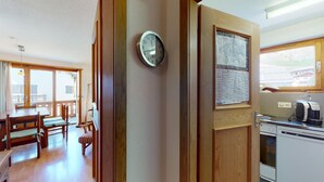A kitchen with wooden cabinets, a clock, a map, and a coffee maker. - 2-room apartment ca. (Celerina/Schlarigna)