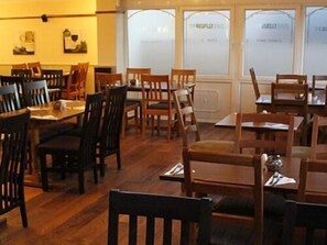 A restaurant with wooden tables and chairs, large windows with frosted glass, and artwork on the walls. - The Begelly Arms (Kilgetty)