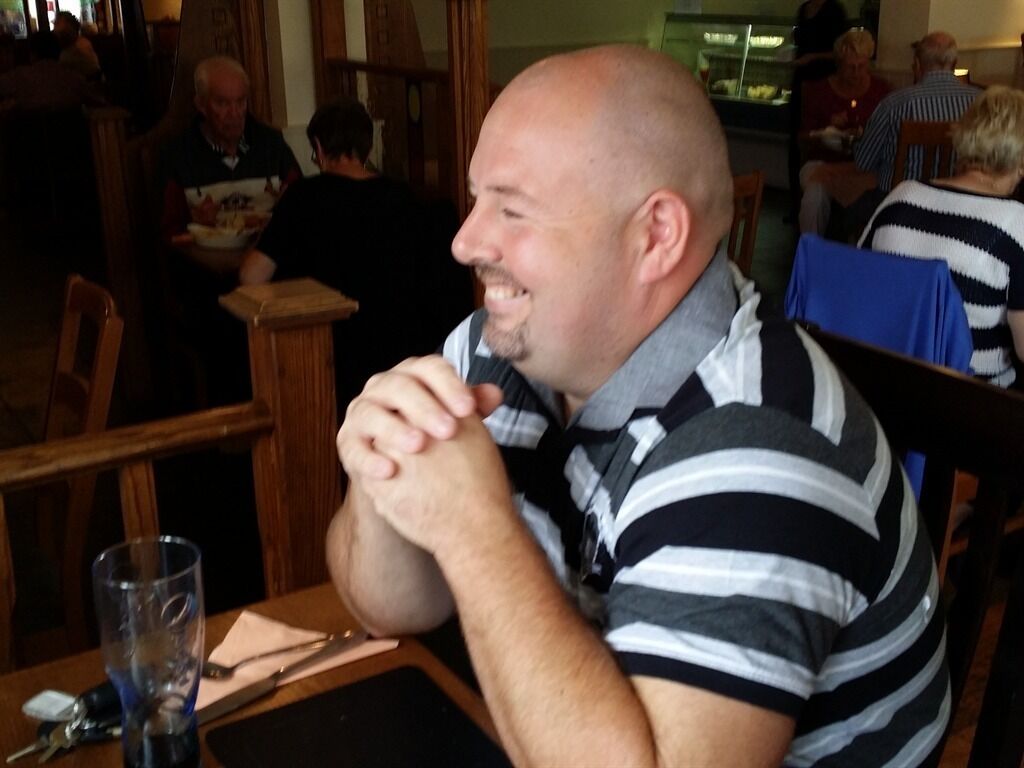 A man sitting at a table in a restaurant with other patrons in the background.