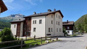A two-story building with a wooden facade and multiple windows, surrounded by a wooden fence and a clear sky. - 4½-room apartment on the second floor, approx. (Celerina/Schlarigna)