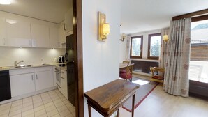 A kitchen with white cabinets, a sink, and a toaster. There is a dining area with a table and chairs, and a window with curtains. - 4½-room apartment on the second floor, approx. (Celerina/Schlarigna)