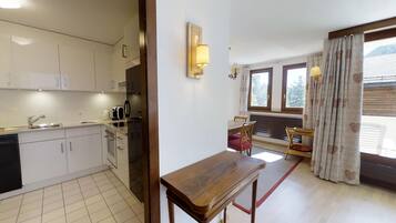 Eine Küche mit weißen Schränken, einem Spülbecken und einem Toaster. Es gibt eine Essecke mit Tisch und Stühlen, sowie ein Fenster mit Vorhängen.