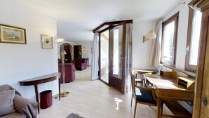 A spacious living area with a wooden floor, a sofa, a dining table with chairs, and a large window providing natural light. - 4½-room apartment on the second floor, approx. (Celerina/Schlarigna)