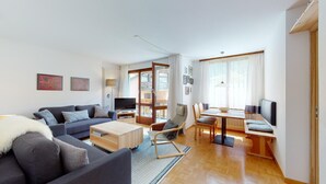 Ein modernes Wohnzimmer mit Sofa, Couchtisch, Fernseher und einem Essbereich mit Tisch und Stühlen.