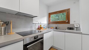 Uma cozinha moderna com eletrodomésticos de aço inoxidável, uma janela com vista para árvores e uma cafeteira sobre a bancada.