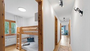 Quarto com beliche, janela, piso de madeira e corredor que dá para uma varanda.