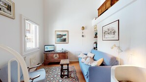 A cozy living room with a blue sofa, a wooden cabinet, a television, and a patterned rug. - Spacious and quiet 2-room apartment on two floors, 45m2, facing north. (Sils/Segl Maria)