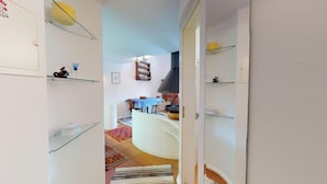 A narrow hallway with glass shelves on both sides, leading to a dining area with a table and chairs. - Spacious and quiet 2-room apartment on two floors, 45m2, facing north. (Sils/Segl Maria)