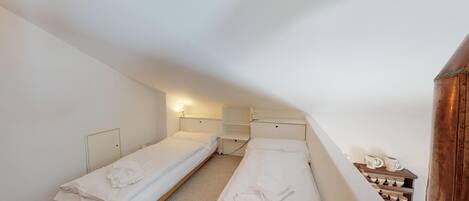 A small, dimly lit room with two single beds, a wooden cabinet with dishes, and a sloped ceiling.
