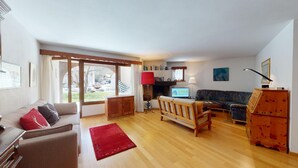 Ein geräumiges Wohnzimmer mit Holzboden, einer Couch, einem roten Teppich, einem Fernseher und einem Kamin.