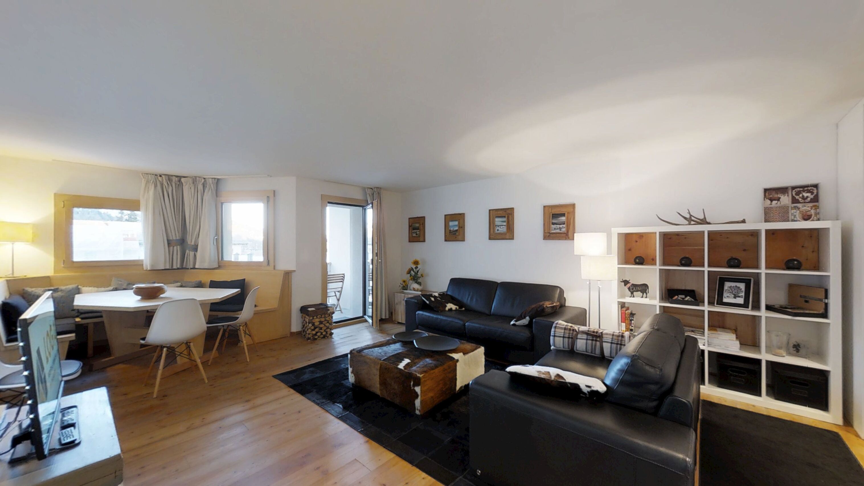 Ein Wohnzimmer mit einer Couch, einem Couchtisch, einem Esstisch mit Stühlen und einem Bücherregal.