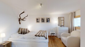 A bedroom with a bed, a desk, a chair, a mirror, and wall-mounted deer antlers.