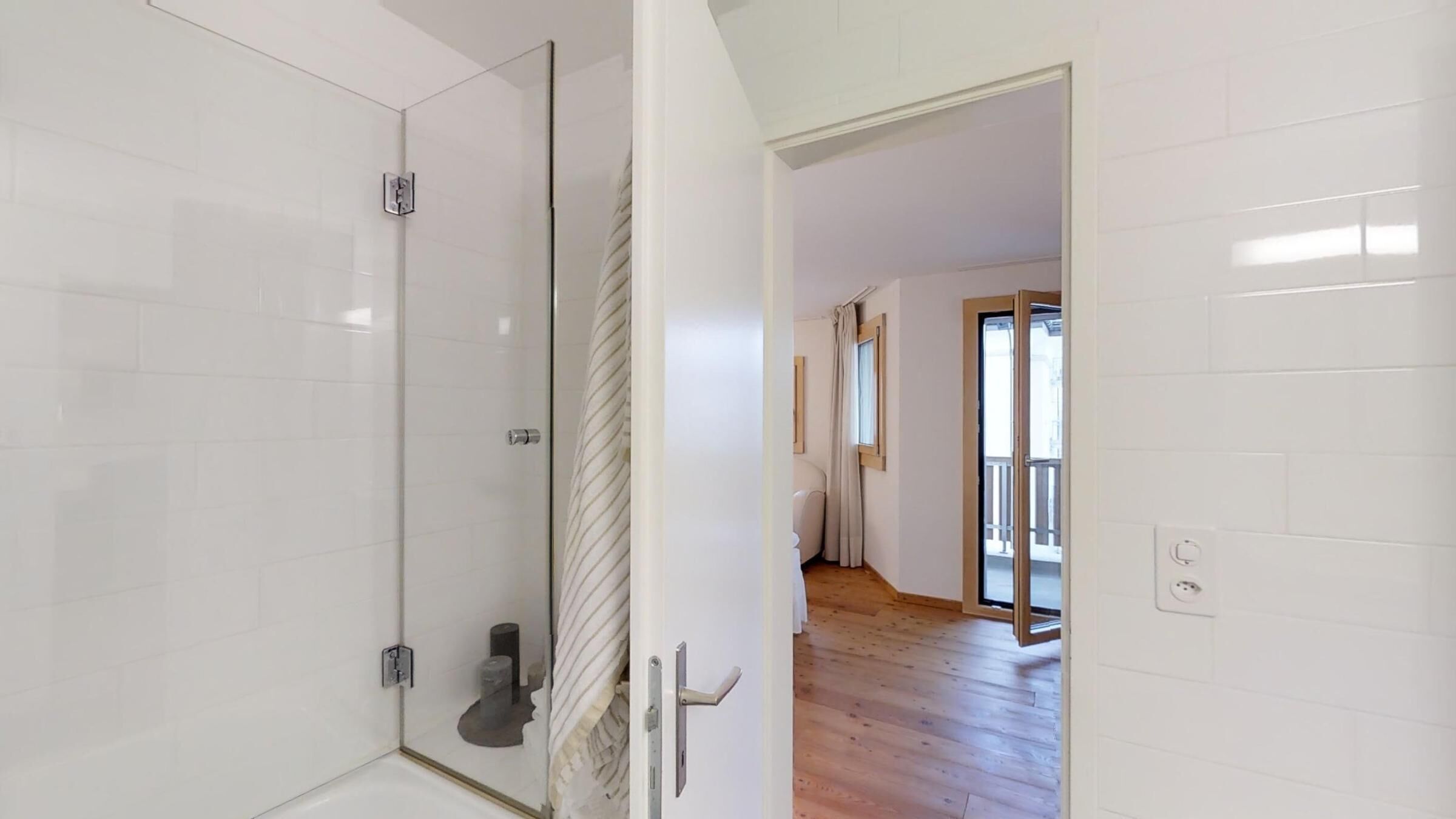 Een moderne badkamer met een douchecabine van glas, een witte betegelde wand en een houten vloer.