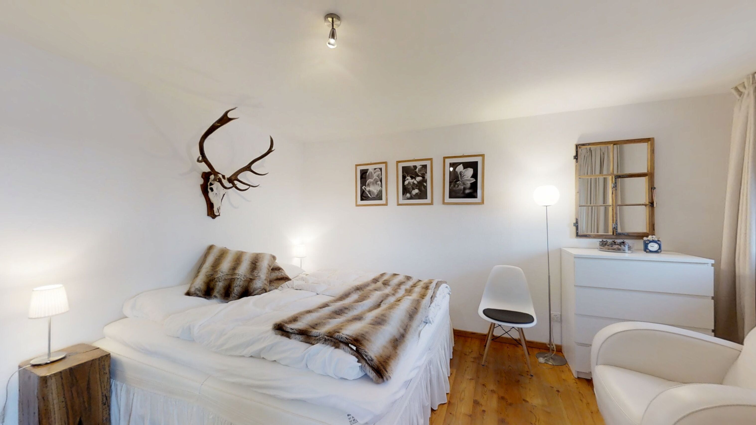 Une chambre à coucher comprenant un lit, un bureau, une chaise, une lampe et des éléments de décoration murale, notamment un crâne de cerf et des tableaux encadrés.