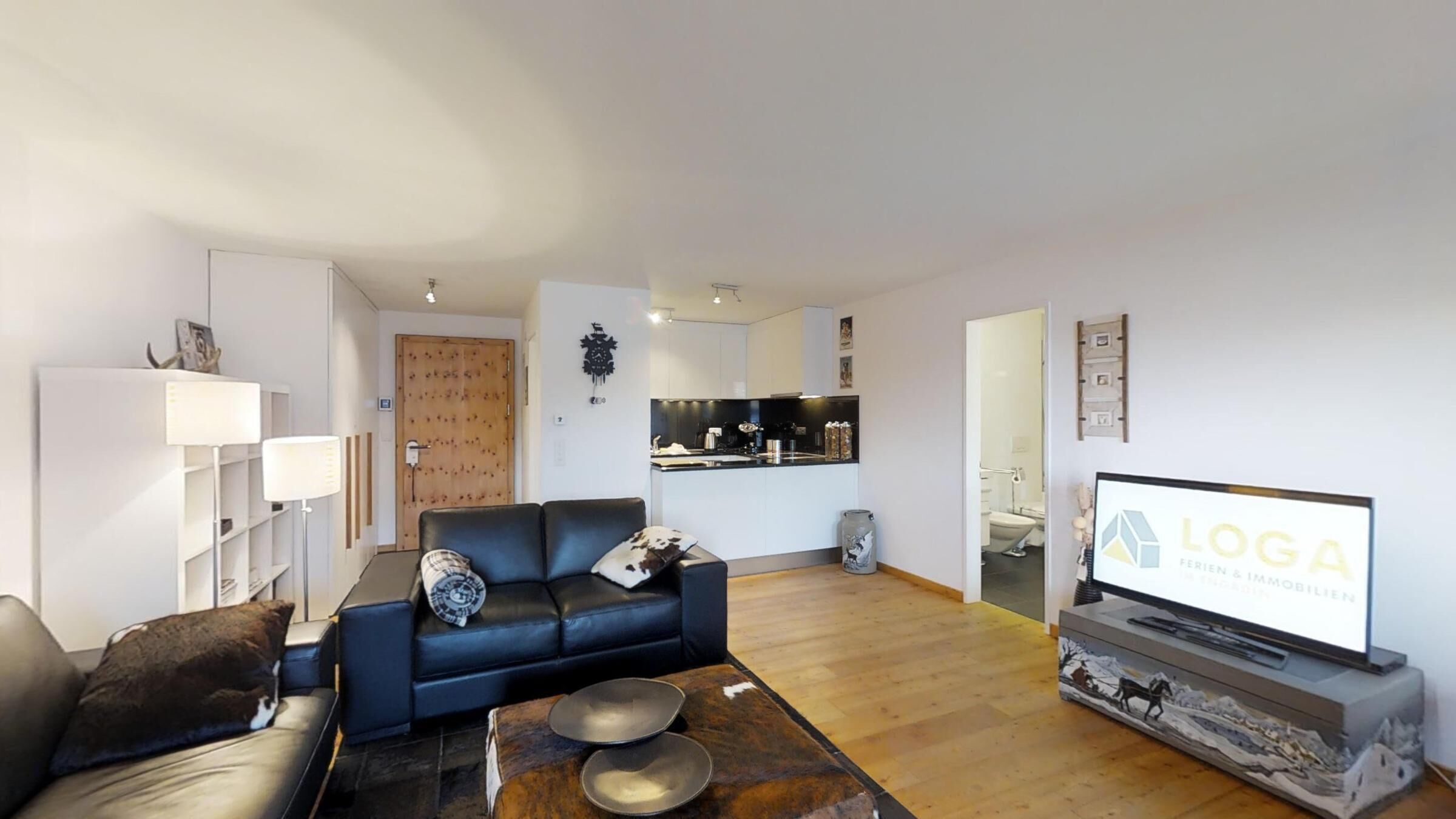 A modern living room with a black leather sofa, a coffee table, and a flat-screen TV.