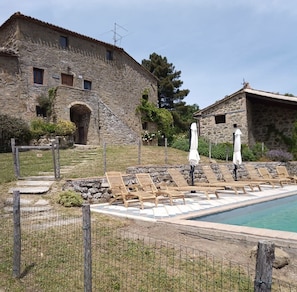 Un bâtiment en pierre doté d’un espace piscine, comprenant des chaises longues et des parasols.