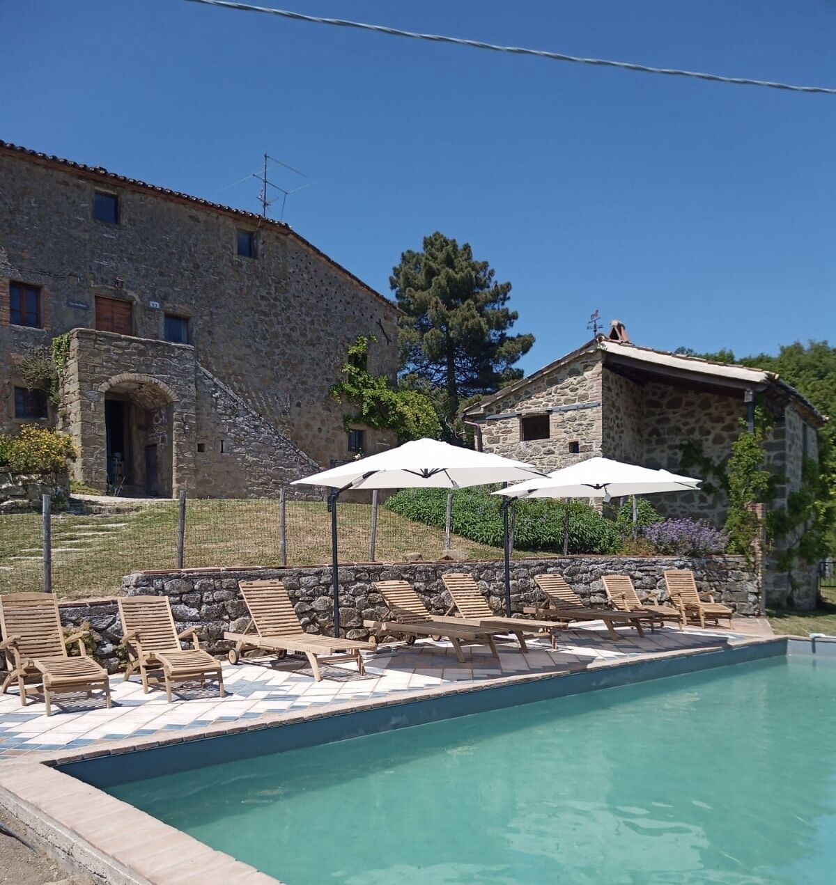 Un bâtiment en pierre doté d’un espace piscine comprenant des chaises longues en bois et des parasols.