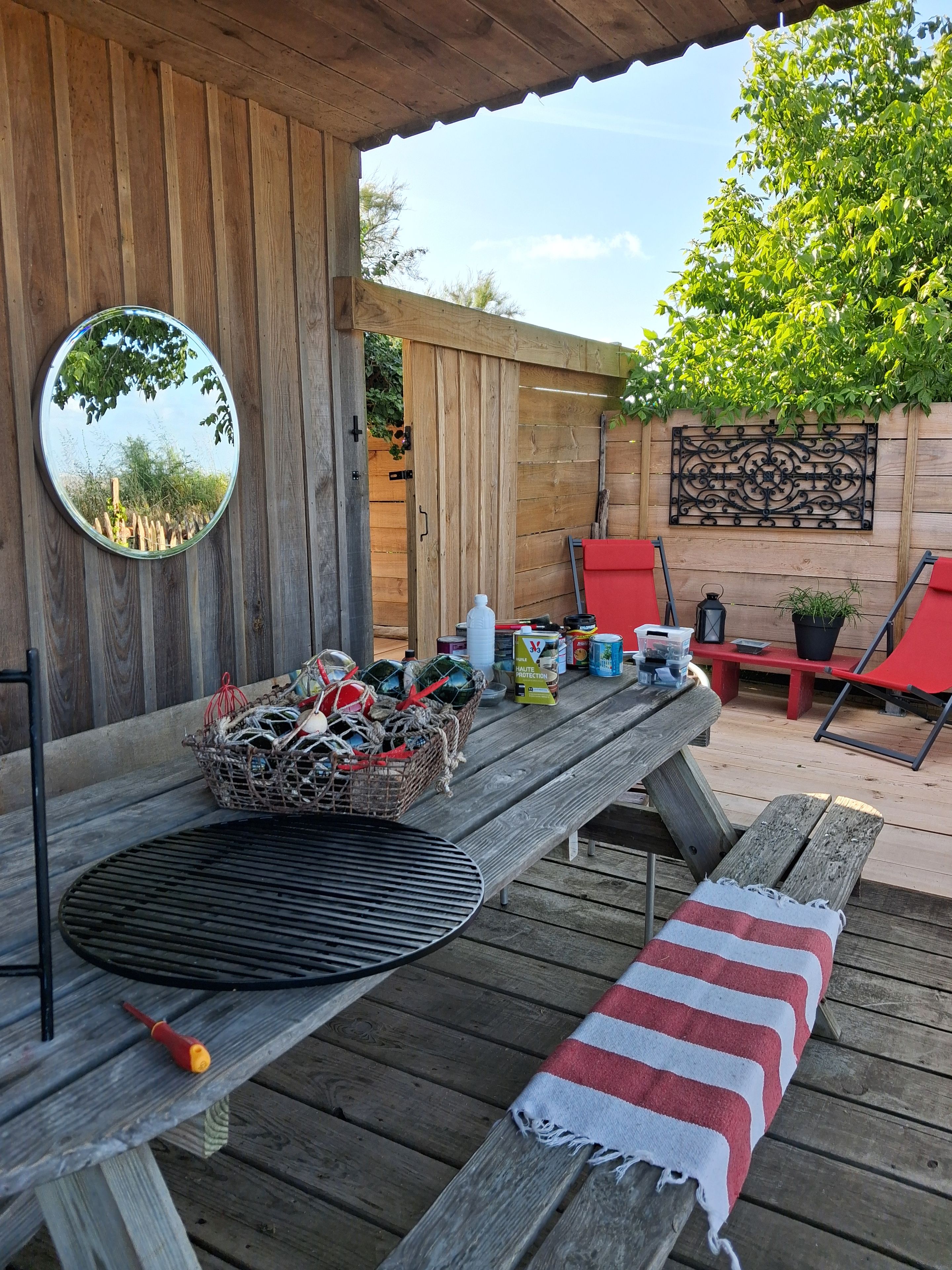 A wooden deck with a grill, a table with various items, red chairs, and a mirror.