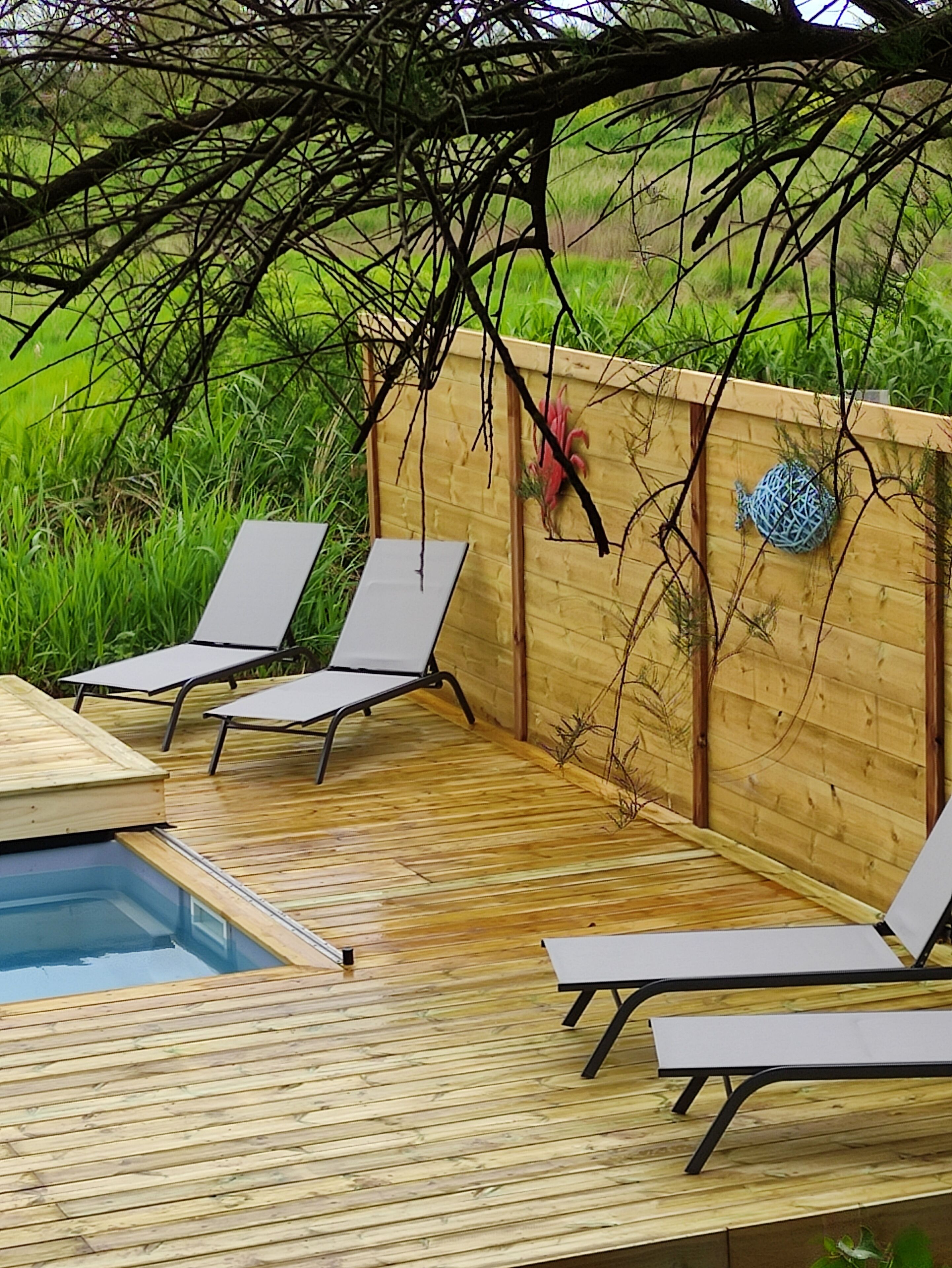 A wooden deck with two lounge chairs and a pool.