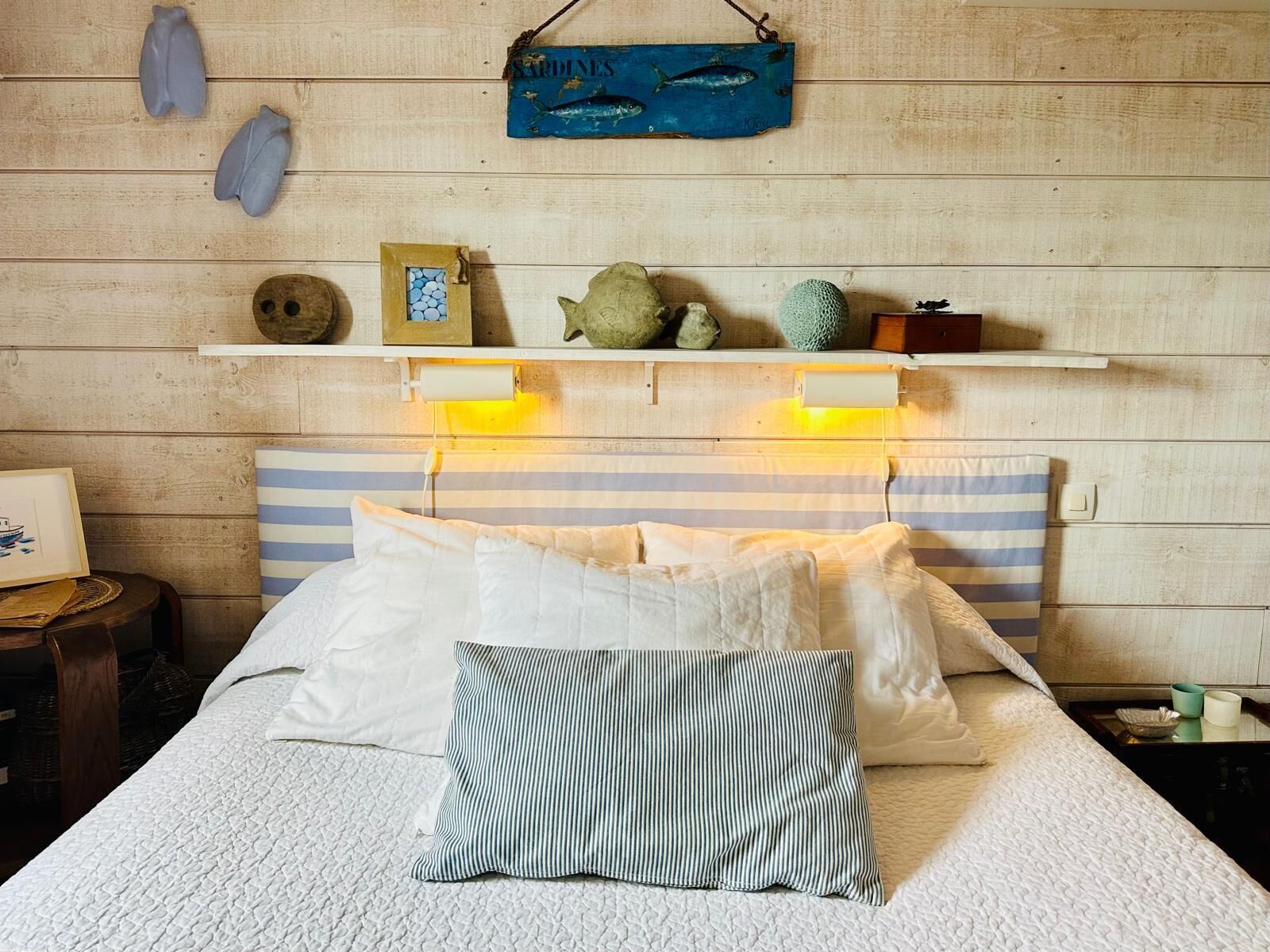 A bed with white and striped bedding, a shelf above with decorative items, and a wooden wall.
