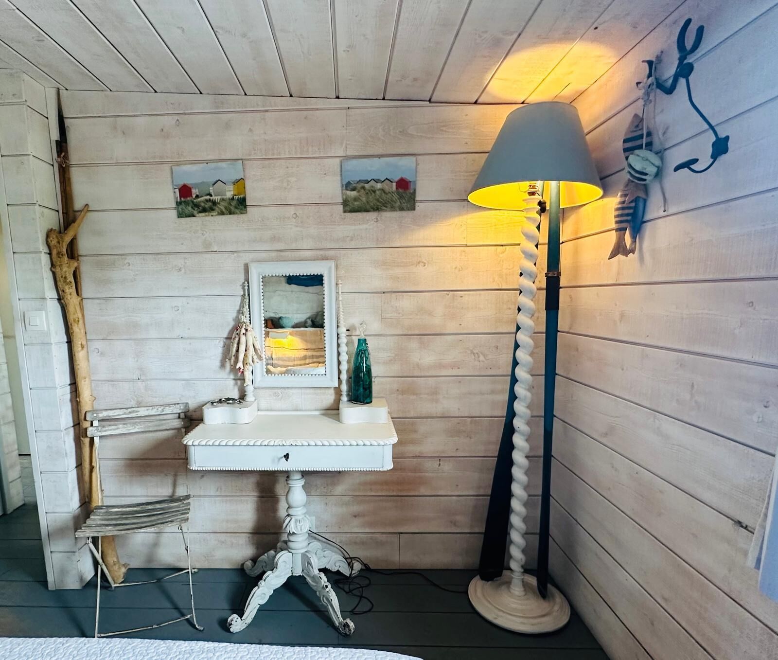 Una camera rustica con una parete in legno, un comò bianco con specchio, una lampada e un piccolo ripiano con oggetti decorativi.