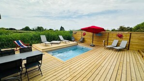 Una terraza de madera con un jacuzzi, sillas de descanso y una mesa con sillas.