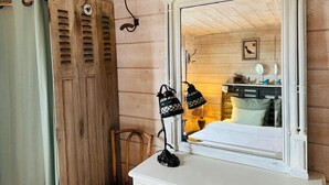 Una habitación con techo de madera, un tocador blanco con espejo y una ventana con contraventanas.