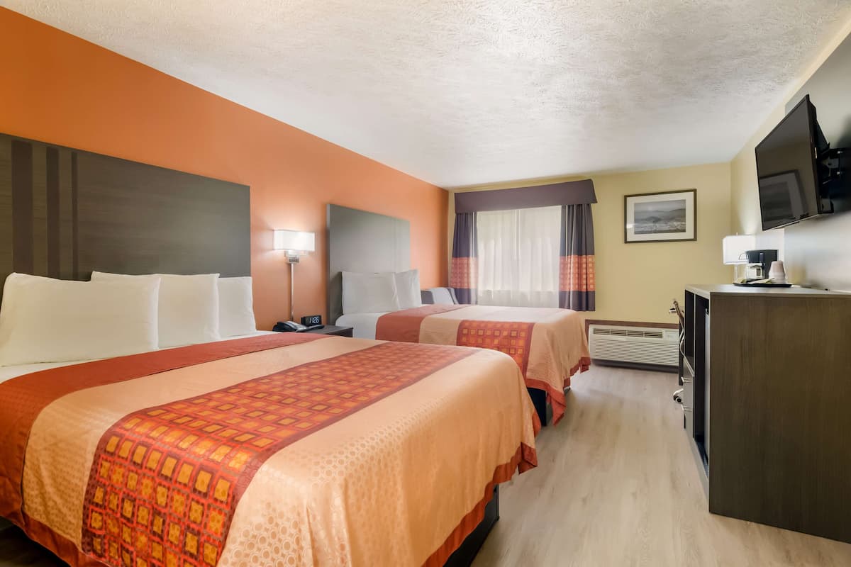 Ein Hotelzimmer mit zwei Betten, einem Schreibtisch, einem Fernseher und einem Fenster mit Vorhängen.