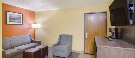 Una habitación con sofá, sillón y reposapiés, televisor de pantalla plana y una puerta.