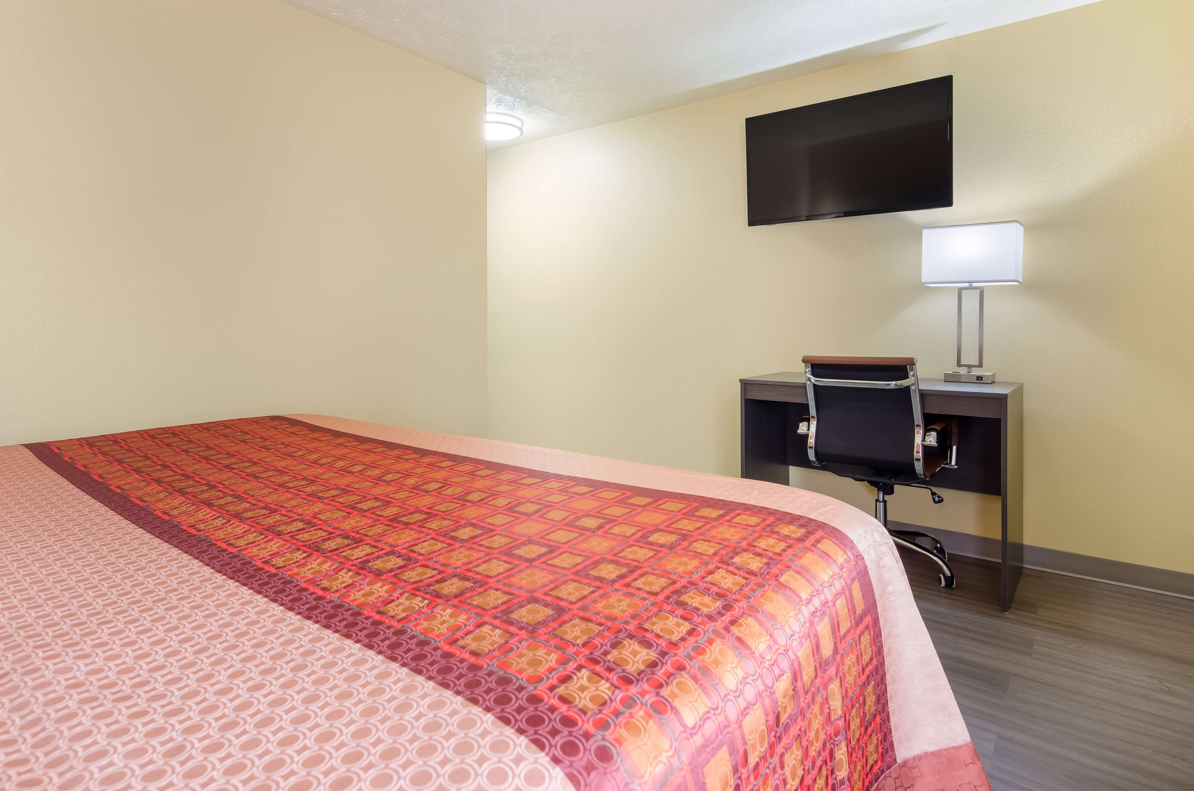 Quarto de hotel com uma cama, uma mesa, uma cadeira, uma televisão e um abajur.