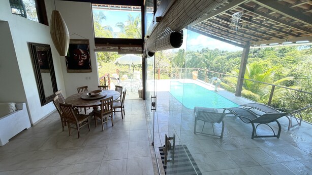 A dining area with a table and chairs, a large window, and a view of a swimming pool and lush greenery.