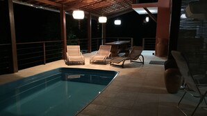 An outdoor swimming pool with lounge chairs and a pergola with hanging lights.
