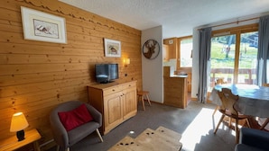 Ein gemütliches Zimmer mit Holzwänden, einem Fernseher, einer Couch, einem Esstisch und einer Küchenzeile.