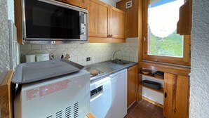 A compact kitchen with wooden cabinets, a built-in microwave, a dishwasher, and a window with a view of greenery.