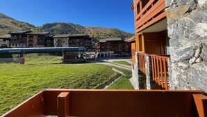 A hotel with a stone facade, a balcony, and a view of a train and mountains in the background.