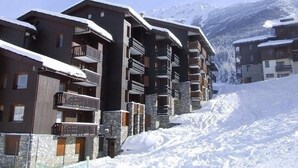 Ein schneebedecktes Bergresort mit mehrstöckigen Gebäuden, Balkonen und Steinfassaden.