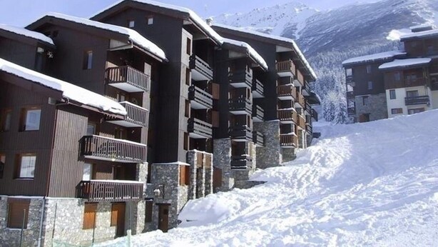 A snow-covered mountain resort with multi-story buildings featuring balconies and stone facades.