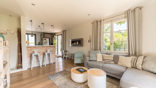 Een moderne woonkamer met een grijze bank, twee witte bijzettafeltjes, een houten salontafel en een schouw met bakstenen.